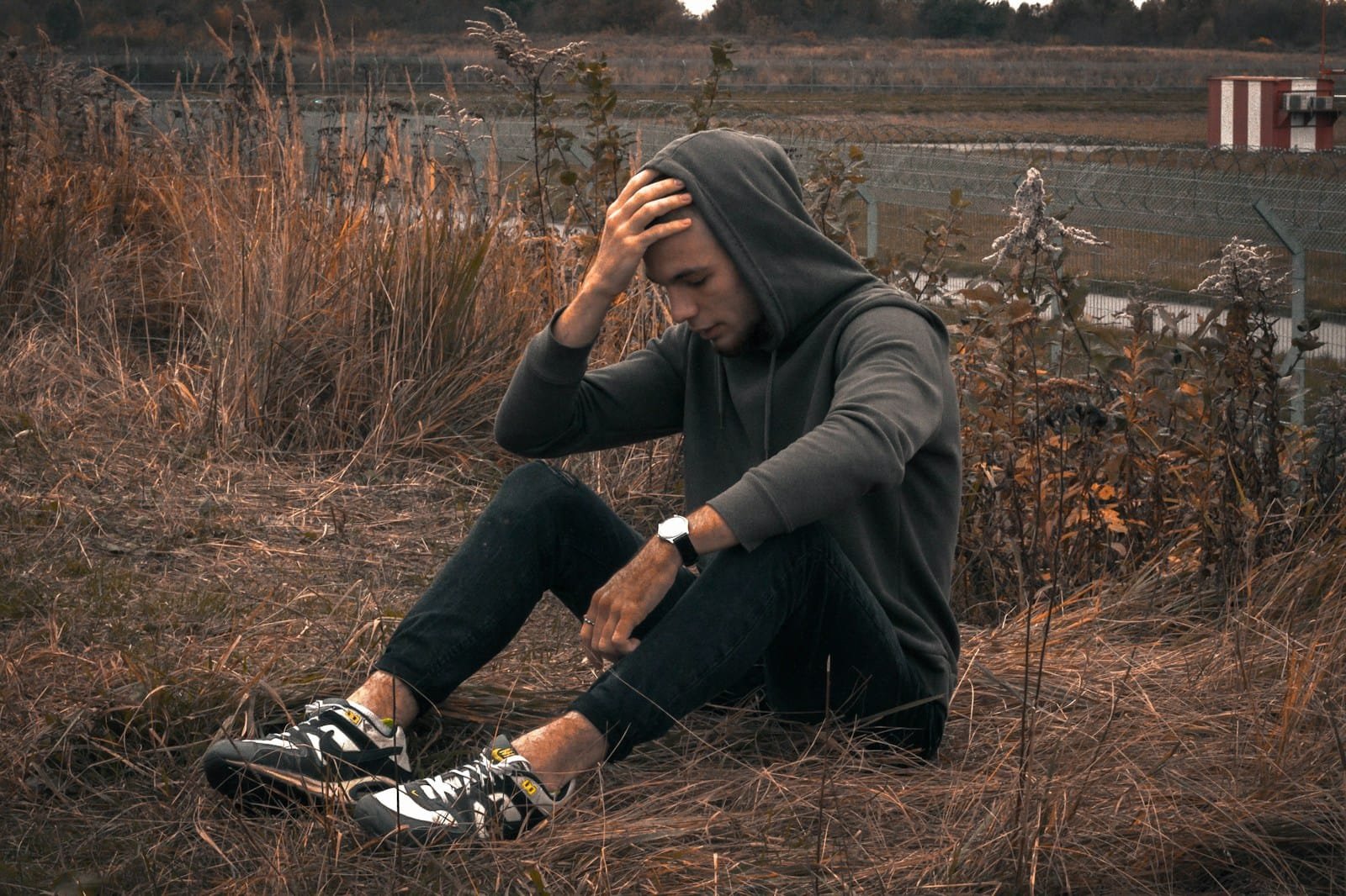man in black jacket and black pants sitting on brown grass field during daytime