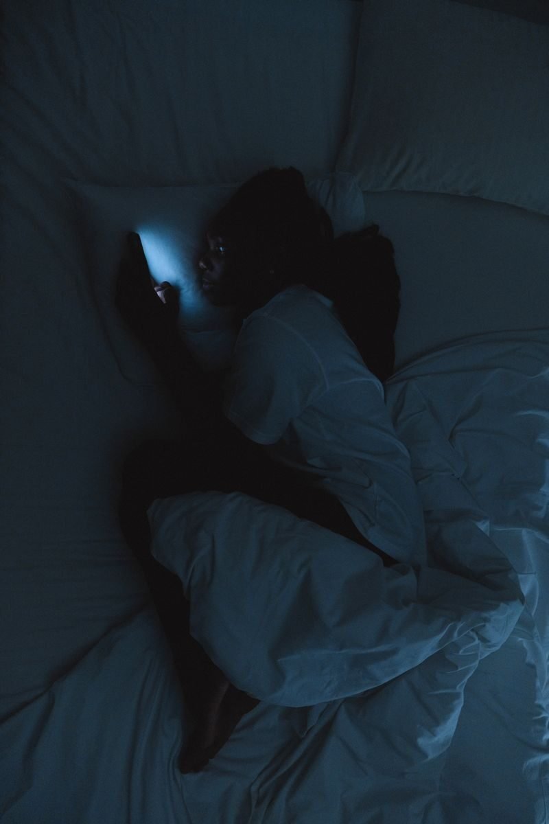 A woman lying in bed at night using a smartphone in a dark room.