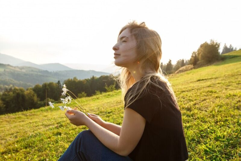 beautiful-blonde-woman-enjoying-mountains-view-holding-camomiles_176420-4166