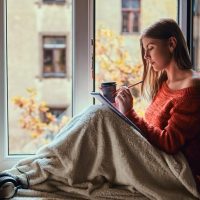 beautiful-girl-warm-sweater-covered-her-legs-with-blanket-makes-notes-her-notebook-sitting-window-sill-open-window_613910-20252