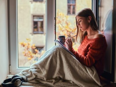 beautiful-girl-warm-sweater-covered-her-legs-with-blanket-makes-notes-her-notebook-sitting-window-sill-open-window_613910-20252