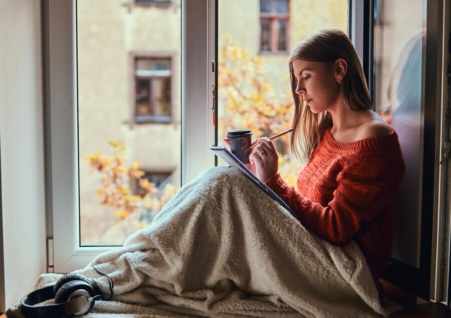 beautiful-girl-warm-sweater-covered-her-legs-with-blanket-makes-notes-her-notebook-sitting-window-sill-open-window_613910-20252