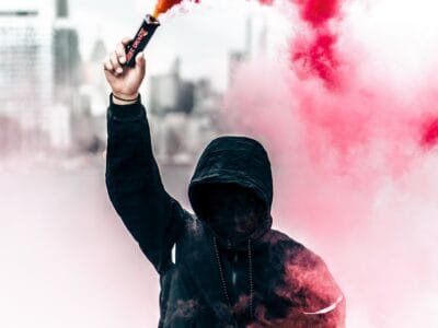 person wearing black and red hoodie holding smoke bomb