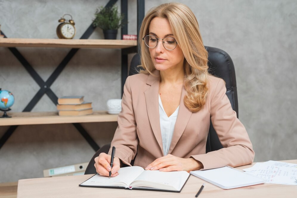 blonde-young-businesswoman-writing-diary-with-pen-office_23-2148029077