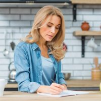blonde-young-woman-writing-with-pen-notebook-wooden-table_23-2148029224