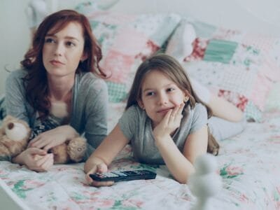 Mother and daughter watch television together on the bed.