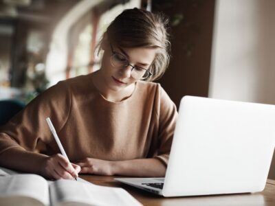 hardworking-focused-woman-trendy-glasses-concentrating-writing-essay-sitting-cozy-cafe-near-laptop-working-making-notes-carefully_197531-21320