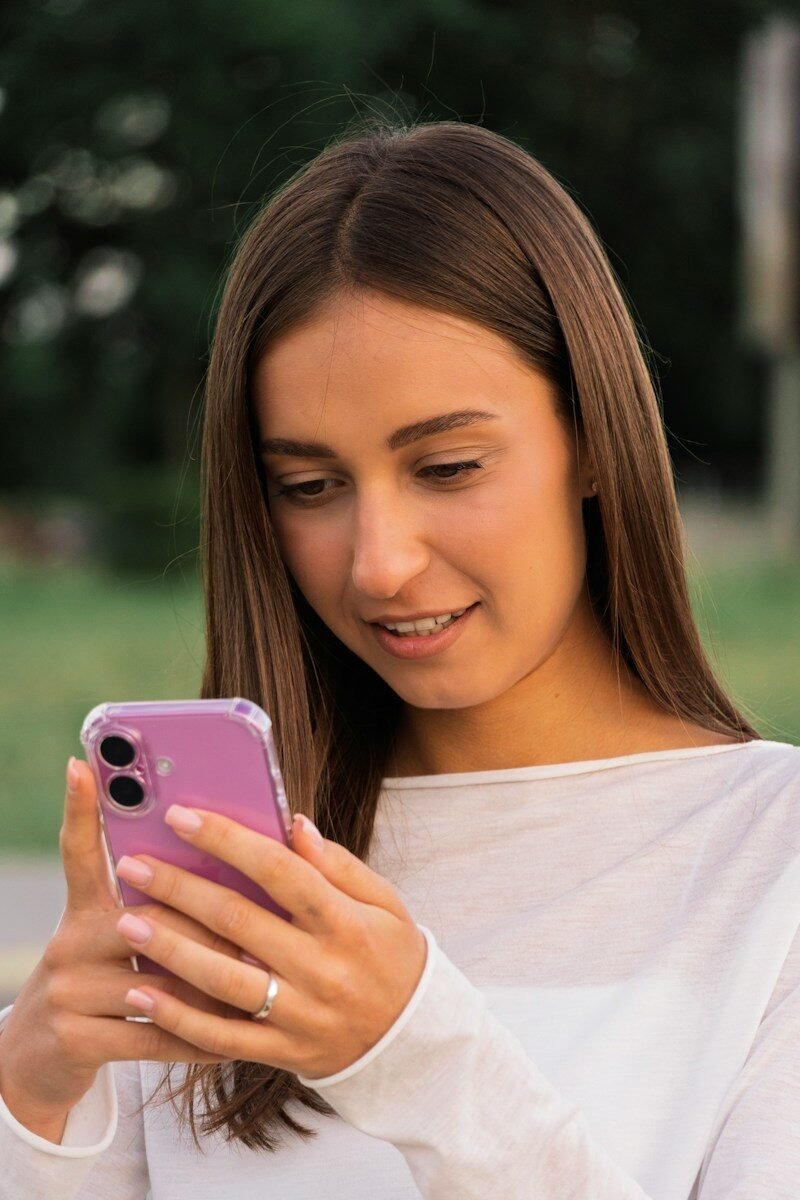 A young woman smiling while looking at her purple smartphone