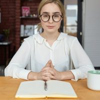 people-business-lifestyle-occupation-concept-serious-young-female-hr-specialist-wearing-round-eyeglasses-white-blouse-clasping-hands-during-job-interview-sitting-desk-making-notes_343059-3060