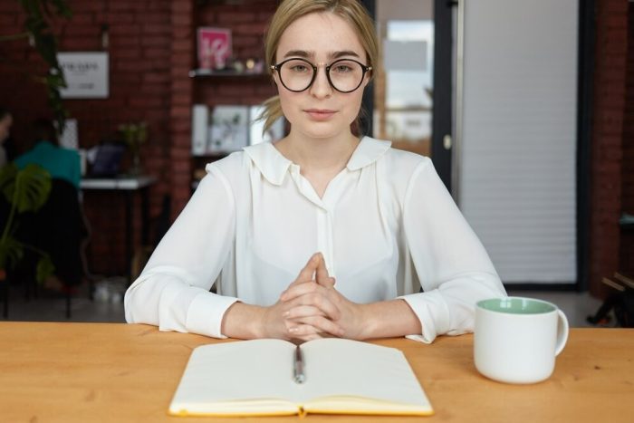 people-business-lifestyle-occupation-concept-serious-young-female-hr-specialist-wearing-round-eyeglasses-white-blouse-clasping-hands-during-job-interview-sitting-desk-making-notes_343059-3060