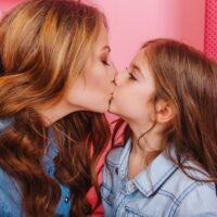 portrait-little-brunette-girl-trendy-vintage-jacket-kissing-her-young-mother-same-outfit-adorable-curly-woman-congratulates-her-daughter-with-birthday-posing-with-giftes-background_197531-25308