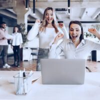 two-young-happy-businesswomen-celebrating-project-success-office