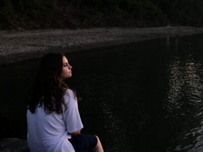 woman sitting on rock while facing lake