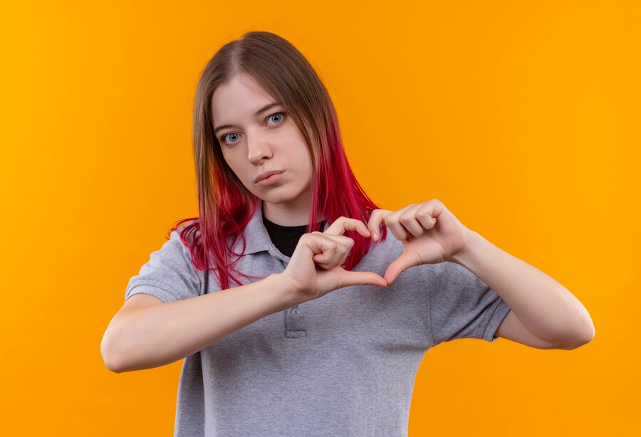 young beautiful woman wearing gray t shirt showing heart gesture isolated yellow wall Straipsniai.lt