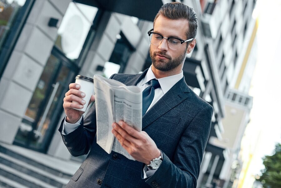 young-businessman-suit-glasses-holding-paper-cup-reading-business-newspaper
