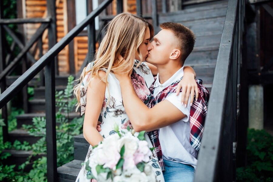 young pretty couple kissing near new wooden home celebrating day their wedding love story Straipsniai.lt